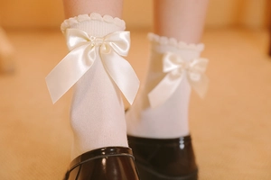 Détail de chaussettes Lolita blanc cassé avec bords à volants et grands nœuds en satin