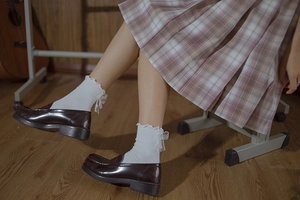 Detail of white Lolita socks with frilly lace and bows paired with brown loafers