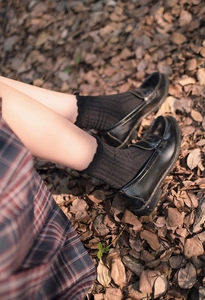 Detail of black mid-calf ribbed socks with ruffled lace edges and pleated skirt styling