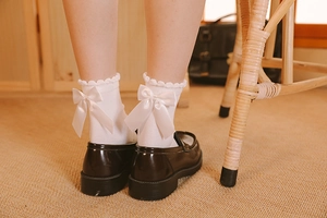 Détail de chaussettes Lolita blanches avec nœud en satin et bordure en dentelle ondulée