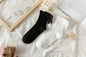 Detail of white and black Lolita socks with mesh bows and ruffled edges on soft bedding