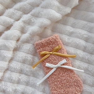 Close-up of pink coral fleece socks with satin bows on a soft white plush background
