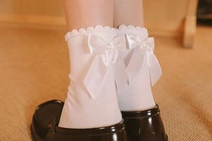 Détail de chaussettes Lolita blanches avec bords dentelés et nœuds en satin au dos