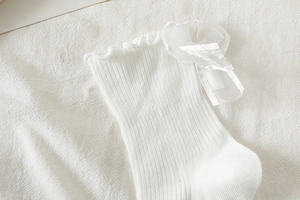 Close-up of white Lolita socks featuring ruffled edges and large sheer ribbon bows