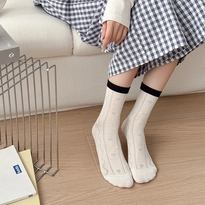 Detailansicht der weißen Herzmuster-Socken mit schwarzen Rippbündchen am Modell