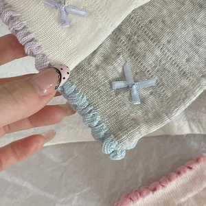 Detail of white and gray cotton knit socks featuring ruffled edges and ribbon bows