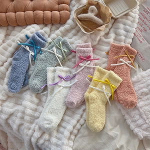 Flat lay of colorful coral fleece socks with double bow ribbons on plush white carpet