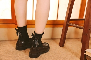 Détail de chaussettes hautes noires avec volants et grand nœud en satin avec mocassins