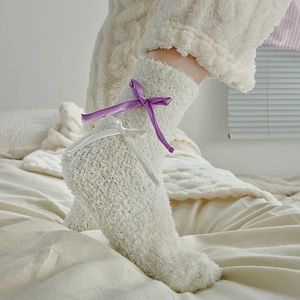 Detail of cream plush socks featuring purple satin bows and warm coral fleece texture