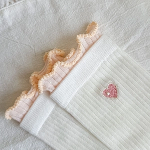 Detail of white ribbed socks with pink ruffled cuffs and heart embroidery