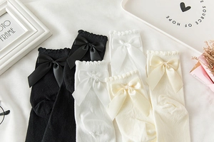 Détail de chaussettes hautes Lolita avec nœuds en soie et bords en dentelle ondulée