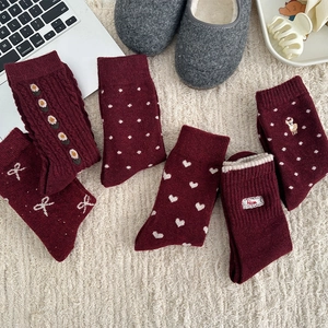 Five pairs of cozy burgundy wool socks with bows and embroidery on white carpet