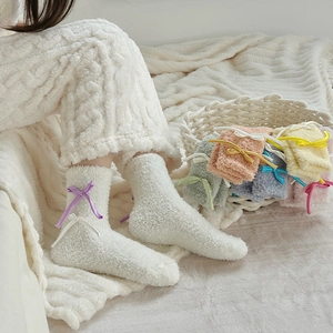 Detail of soft coral fleece socks with colorful silk bows on warm knitted blanket