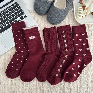 Five pairs of warm burgundy wool socks with bow and heart patterns on white plush rug