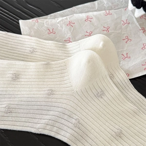 Detailed macro view of white ribbed cotton socks featuring grey bow motifs and lace trim