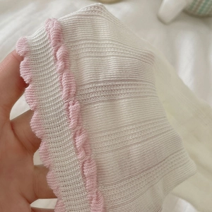 Macro detail of white ribbed socks featuring delicate pink lettuce trim and soft texture