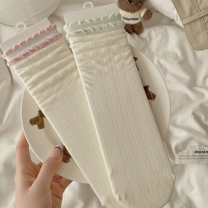 Detailed close-up of white ribbed crew socks featuring pastel pink and green ruffle trim
