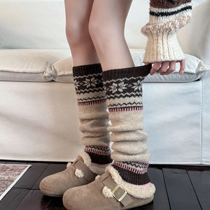 Close-up of beige knit leg warmers with snowflake patterns and plush slippers