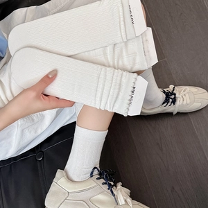 Detail of white knit crew socks featuring delicate cable patterns and ruffled cuff design