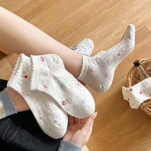 Close-up of white cotton socks with lace trim and small colorful flower embroidery