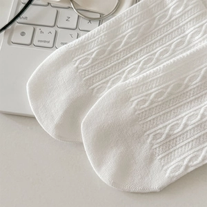 Close-up of white cable knit socks with cotton texture on a minimal desk background