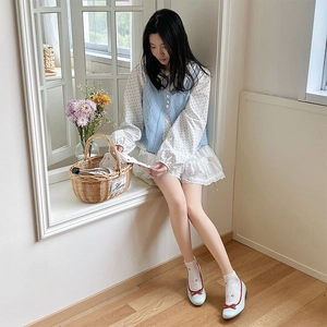 Detail of white lace socks with red bow and blue knit vest on a model in a bright room