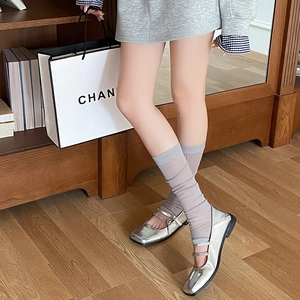 Detail of silver patent leather Mary Jane shoes with grey ribbed mesh leg warmers