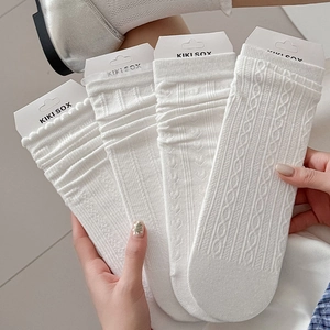 Close-up of four white cable-knit cotton socks with textured patterns and brand packaging