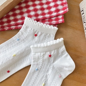 Close-up of white lace socks with heart hollows and colorful dots on wood background