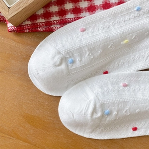 Detailed knit texture of white cotton socks featuring heart patterns and colorful pom-poms