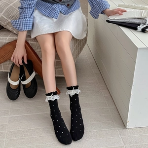 Détail de chaussettes noires à pois avec bordure en dentelle blanche et nœuds en ruban