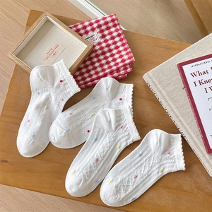 Close-up of white ankle socks with rainbow polka dots and ruffled hem on a wooden table