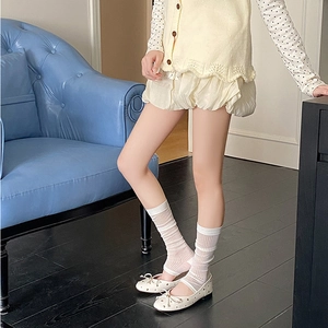Cream flat Mary Jane shoes with bow and pearl accents worn with striped leg warmers