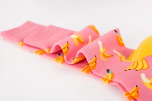 Detail of pink crew socks featuring vibrant yellow banana patterns on white background