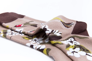 Detail of knitted cotton sock featuring white floral and bird patterns on khaki fabric