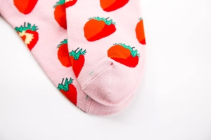 Close-up of pink knit cotton socks featuring red strawberry pattern with green leaves