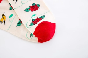 Detailed view of knitted socks with red rose and swallow patterns on cream fabric