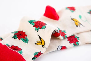 Macro shot of knitted mid-calf socks with red roses and swallow patterns on beige fabric