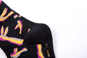 Detail of black cotton socks featuring purple and yellow abstract bird patterns and knit texture