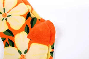 Macro view of bright orange cotton sock featuring yellow flower patterns and knit texture