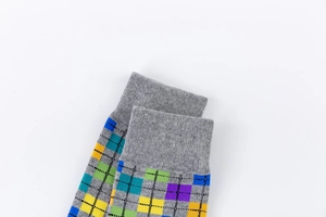 Detail of colorful geometric plaid mid-calf sock with grey ribbed cuff and knit texture