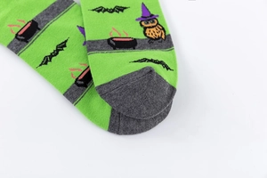 Detail of green Halloween socks featuring owl with witch hat and bat knitting patterns