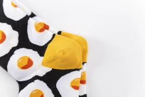 Close-up of black cotton socks featuring yellow fried egg pattern and yellow heel detail