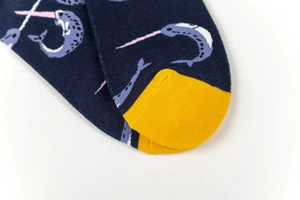 Detail of dark blue crew sock featuring light blue narwhal pattern and yellow toe accent