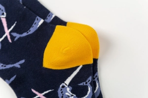 Close-up of a blue cotton sock with yellow reinforced heel and narwhal pattern