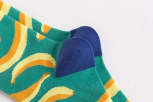 Macro view of green cotton socks with banana pattern and reinforced blue stitching