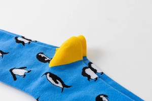 Detail of blue knit sock featuring white penguin patterns and 3D yellow fabric accents