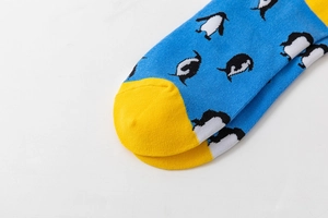 Detail of knitted socks with penguin pattern and yellow contrast toe on blue fabric
