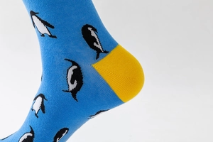 Detail of blue cotton socks with penguin print and yellow heel contrast knitting