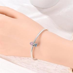 Detail of silver snake chain bracelet featuring a pink and blue enamel flower charm